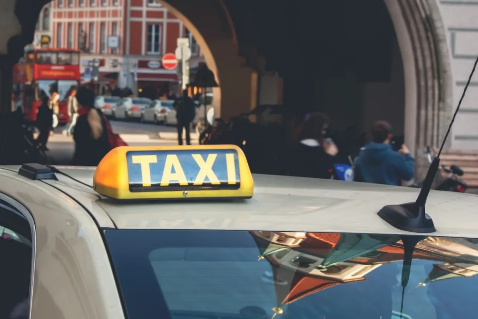 Close-up on yellow and black TAXI sign on top of beige car in central Munich, Germany.